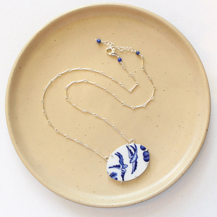 The birds of a feather vintage plate necklace styled on a tan plate to show the adjustable lobster clasp closure