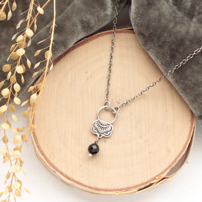 The black tourmaline jolie necklace styled on wood with gray velvet and dried grass