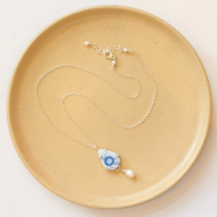 The blue flower and pearl drop vintage plate necklace styled on a tan plate to show the adjustable lobster clasp closure