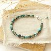 The blue and green gemstone bracelet styled on a tan rock with dried grass