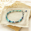 The blue mixed gemstone bracelet styled on a tan rock with linen and dried grass