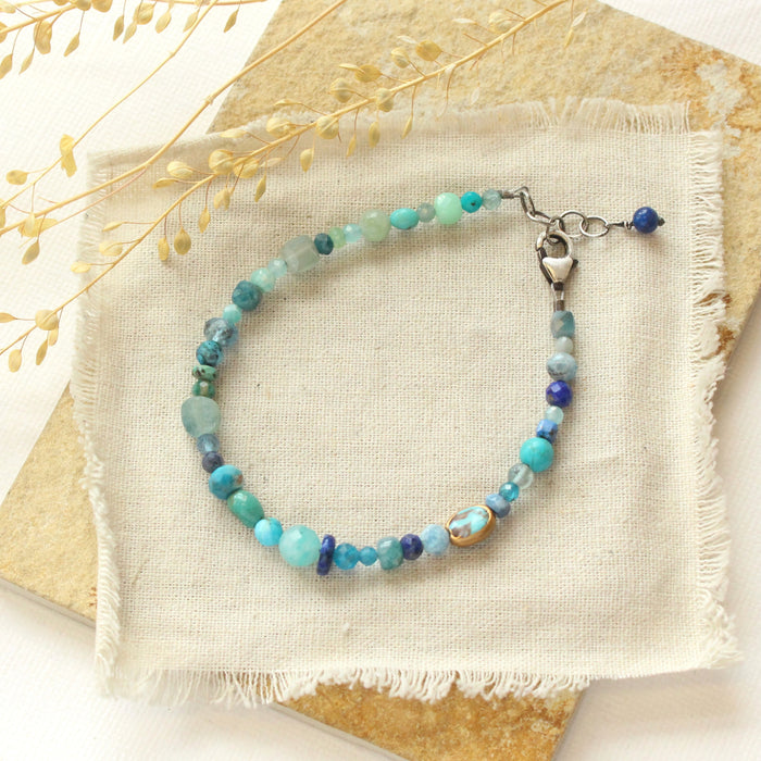 The mixed blue gemstone bracelet styled on a tan rock with linen and dried grass