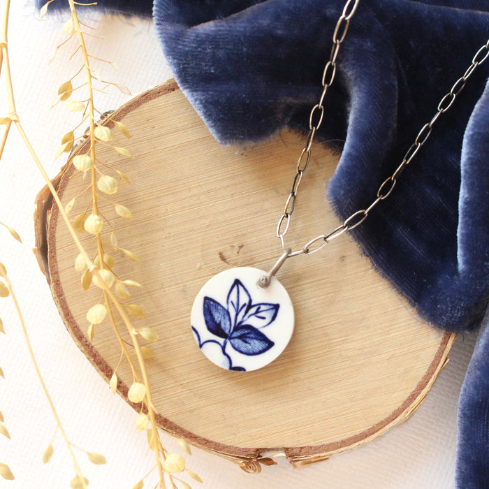 The blue sprig vintage plate necklace styled on wood with blue velvet and dried grass
