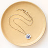 The blue sprig vintage plate necklace styled on a tan plate to show the adjustable lobster clasp closure