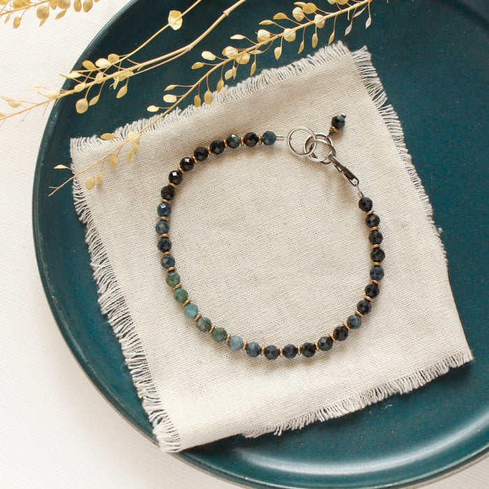 The blue tourmaline and brass bracelet styled on a blue plate with tan linen and dried grass