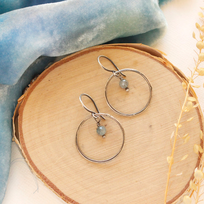 The zircon silver hoop earrings styled on wood with blue velvet and dried grass