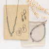 The zircon silver hoop earrings styled with the matching necklace, bracelet, and another pair of earrings on a tan rock with linen and dried grass
