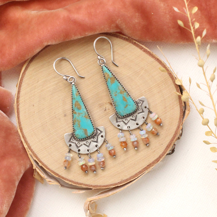 The boho turquoise triangle fringe earrings styled on wood with orange velvet and dried grass