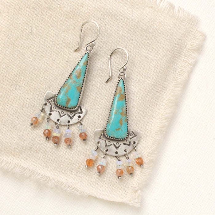 The boho turquoise, sunstone, and opal fringe earrings styled on tan linen