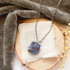 The boulder opal necklace styled on wood with linen, gray velvet, and dried grass