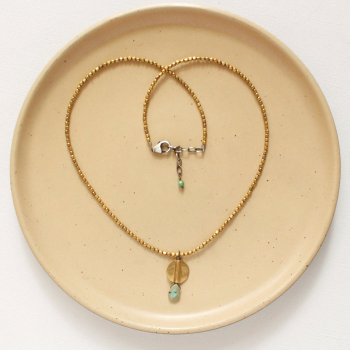 The brass and african jasper drop necklace styled on a tan plate to show the adjustable lobster clasp closure
