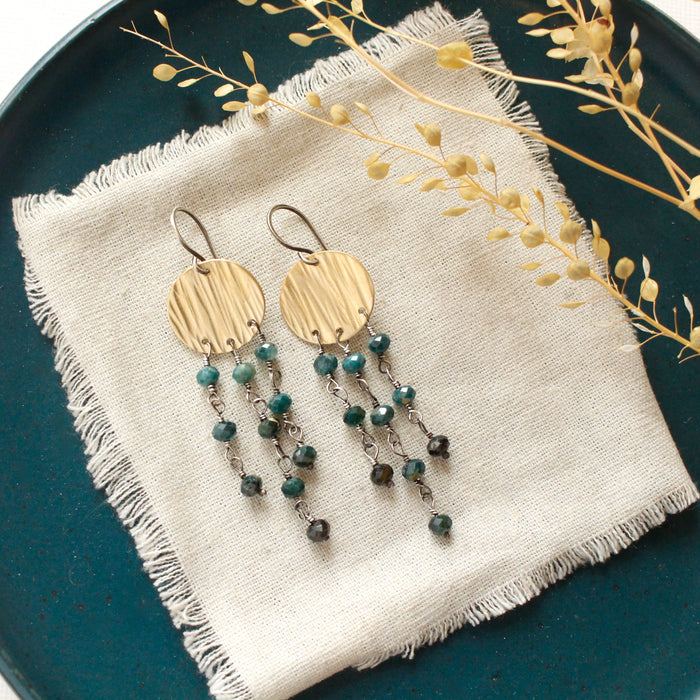 The grandidierite mythos chandelier earrings styled on a blue plate with linen and dried grass