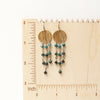 The grandidierite mythos chandelier earrings on a wooden ruler for size reference