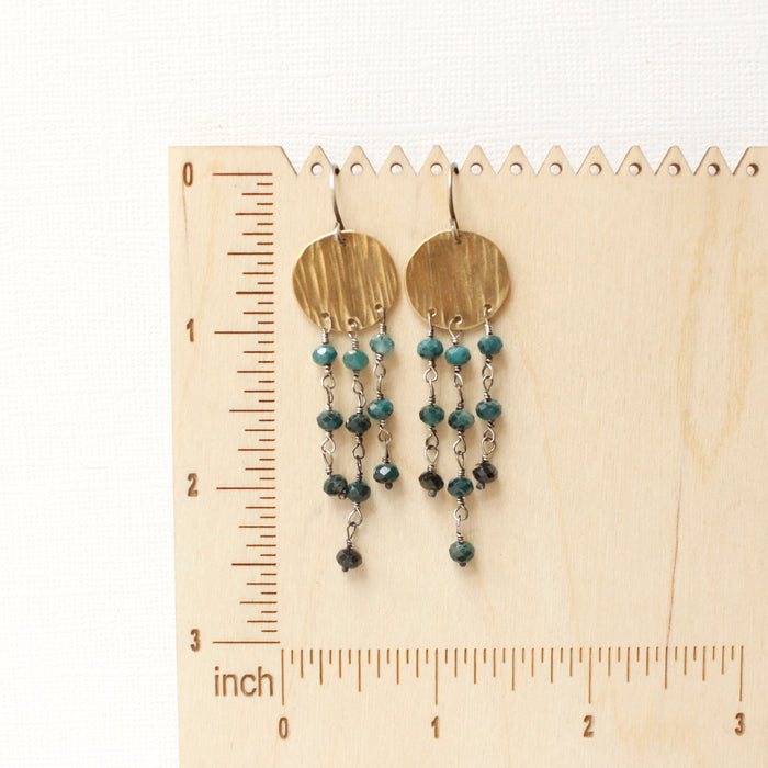 The grandidierite mythos chandelier earrings on a wooden ruler for size reference