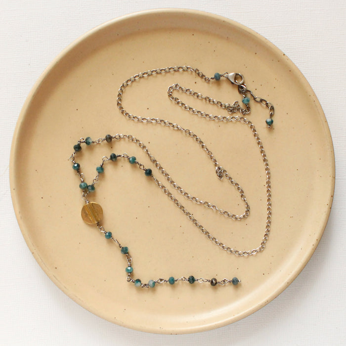 The grandidierite mythos lariat necklace styled on a tan plate to show the adjustable lobster clasp closure