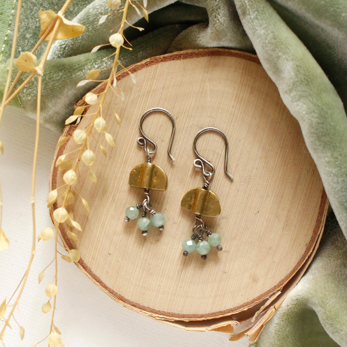 The brass and kyanite mythos earrings styled on wood with green velvet and dried grass