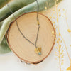 The brass and kyanite mythos necklace styled on wood with green velvet and dried grass