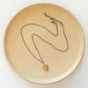 The brass and kyanite mythos necklace styled on a tan plate to show the adjustable lobster clasp closure