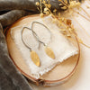 The brass leaf petal earrings styled on wood with linen, gray velvet, and dried grass