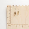 The brass leaf petal earrings on a wooden ruler for size reference