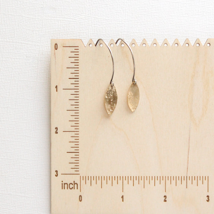 The brass leaf petal earrings on a wooden ruler for size reference