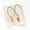 The brass metal earrings styled on tan linen