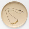 The brass trio mythos necklace styled on a tan plate to show the adjustable lobster clasp closure
