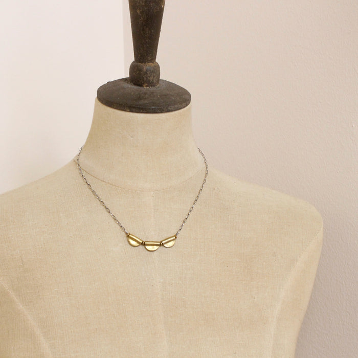 A mannequin wearing the brass trio mythos necklace