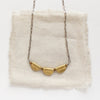 The brass trio mythos necklace styled on tan linen