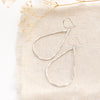 The bright silver forged teardrop hoop earrings styled on tan linen with dried grass