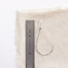 A bright silver forged teardrop hoop earring next to a ruler for size reference
