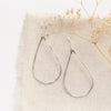 The bright silver forged teardrop hoop earrings styled on tan linen with dried grass