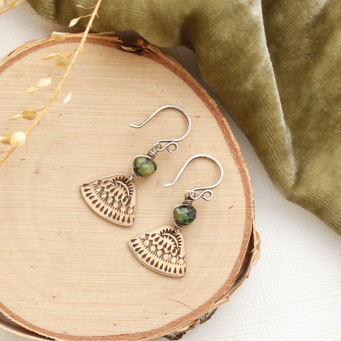The bronze asmi triangle african jasper earrings styled on wood with green velvet and dried grass