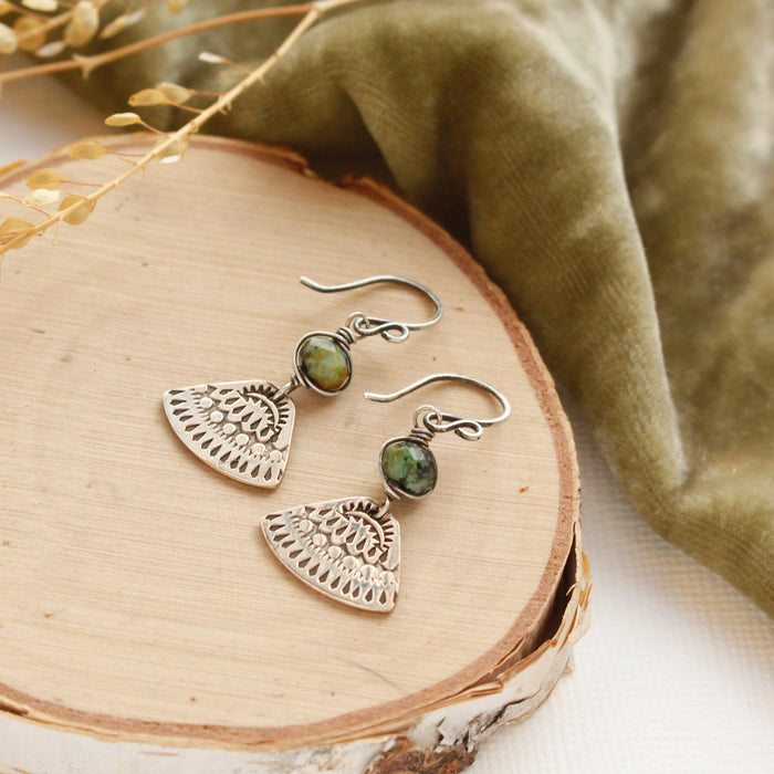 The bronze asmi triangle african jasper earrings styled on wood with green velvet and dried grass