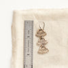 A bronze asmi trio triangle earring next to a ruler for size reference