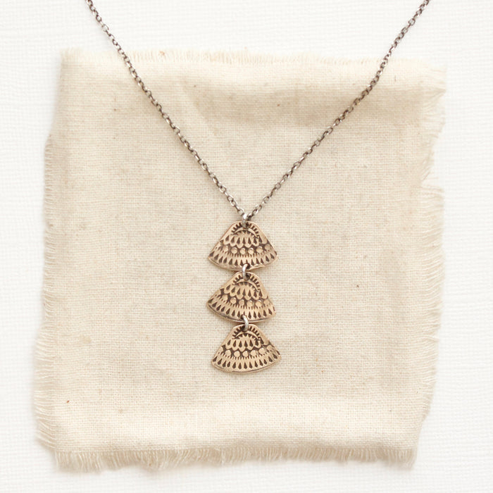The bronze asmi trio triangle necklace styled on tan linen