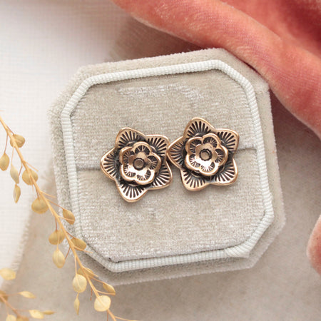 The bronze layered cactus flower post earrings styled on a white velvet box with orange velvet, linen, and dried grass