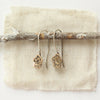 The bronze mini cactus flower lobe hugger earrings styled on a stick with linen