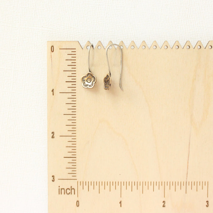 The bronze mini cactus flower lobe hugger earrings on a wooden ruler for size reference