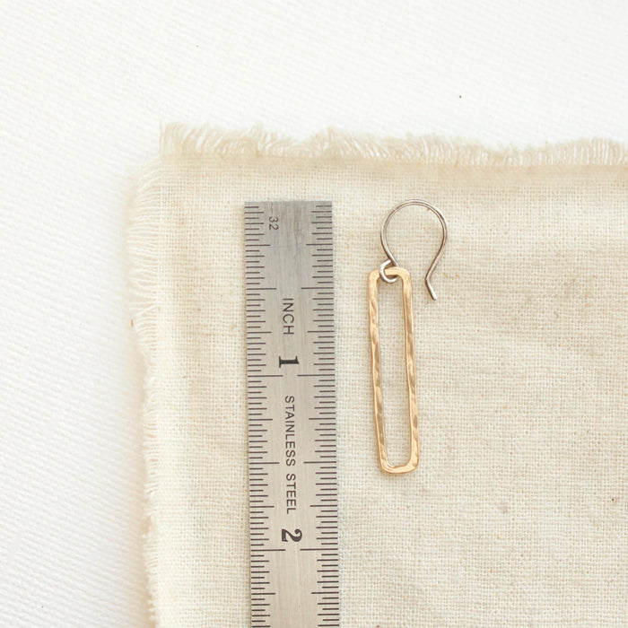 A bronze open bar earring next to a ruler for size reference