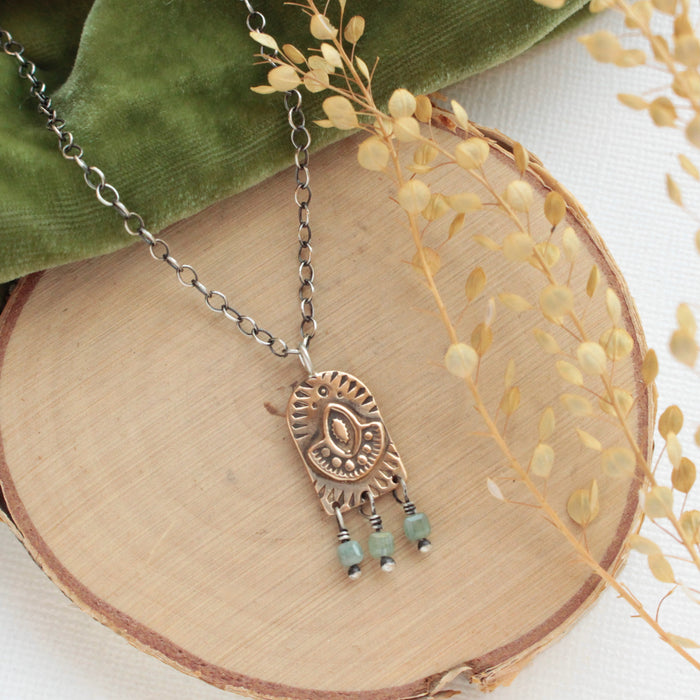 The bronze wanderer arch green apatite necklace styled on wood with green velvet and dried grass