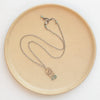 The bronze wanderer arch green apatite necklace styled on a tan plate to show the adjustable lobster clasp closure