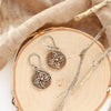 The bronze wanderer coin earrings styled on wood with tan velvet and dried grass
