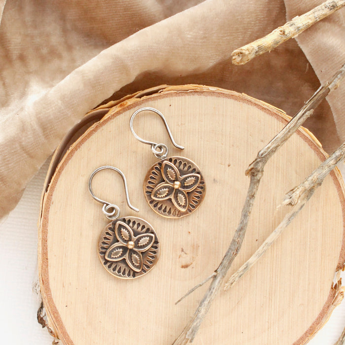 The bronze wanderer coin earrings styled on wood with tan velvet and dried grass