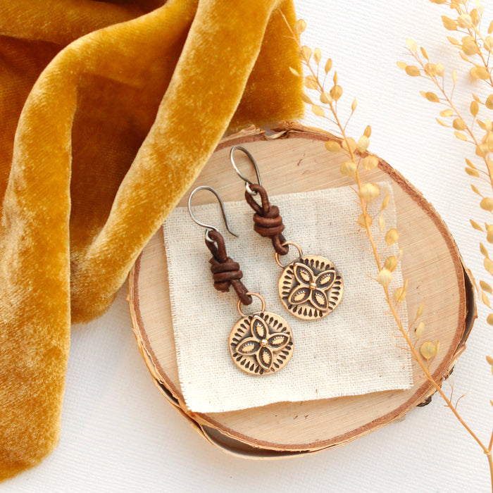 The bronze wanderer coin leather earrings styled on wood with yellow velvet and dried grass