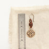 A bronze wanderer coin leather earring next to a ruler for size reference