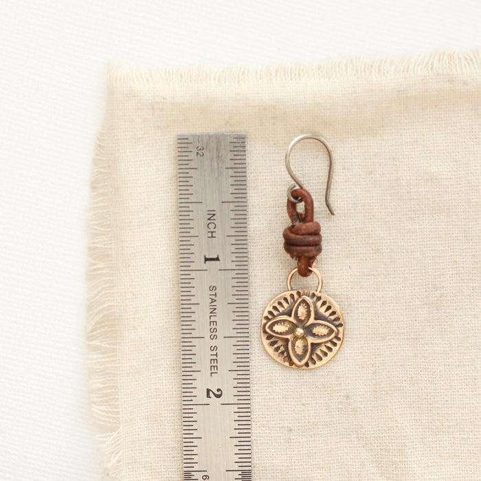 A bronze wanderer coin leather earring next to a ruler for size reference