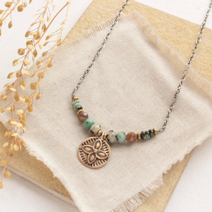 The bronze wanderer coin lona necklace styled on a tan rock with linen and dried grass