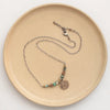 The bronze wanderer lona necklace styled on a tan plate to show the adjustable lobster clasp closure
