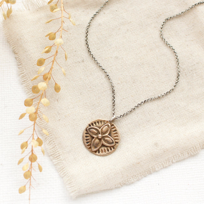 The bronze wanderer coin necklace styled on tan linen with dried grass